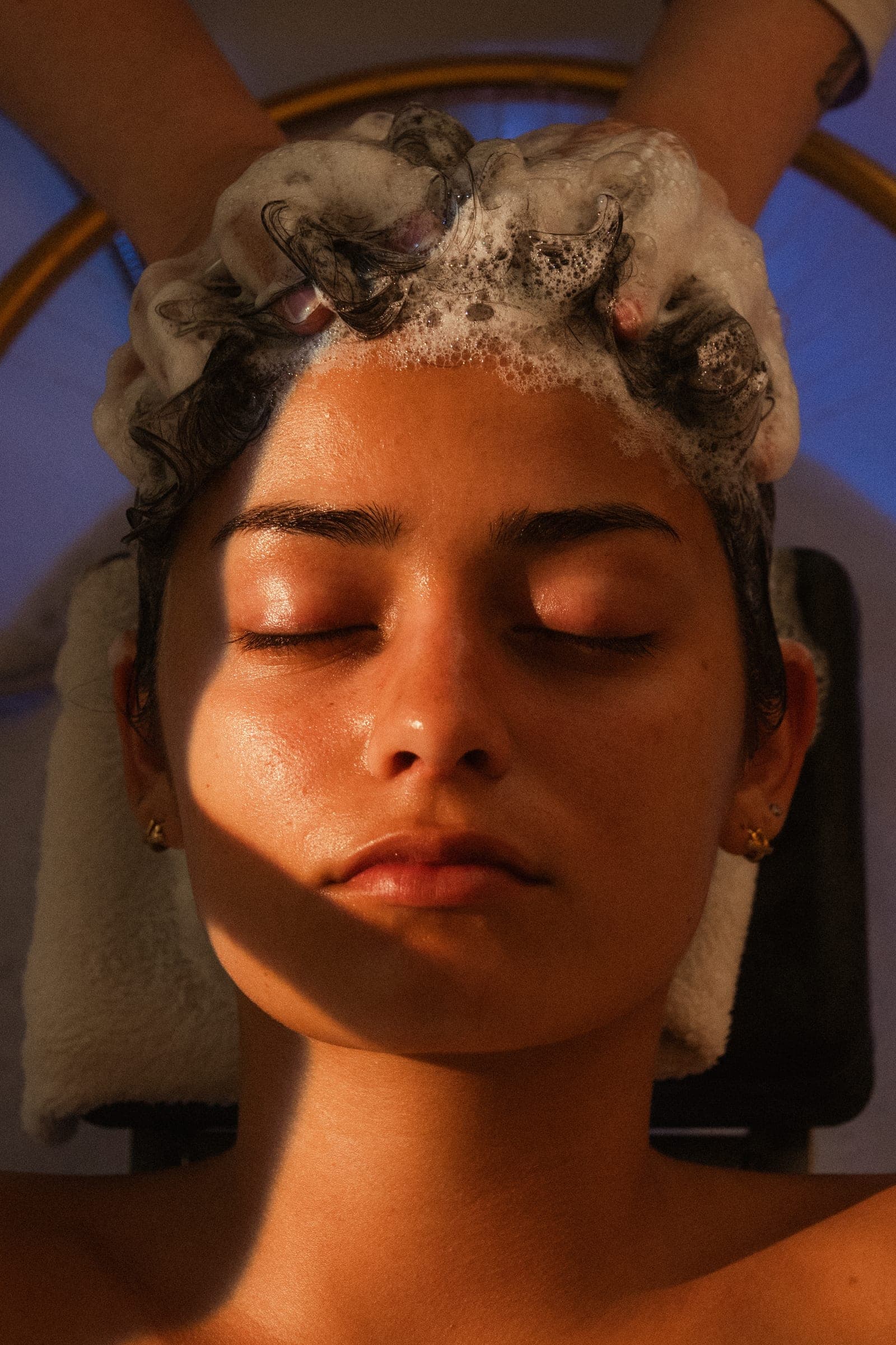 A guest beneath the head spa halo, eyes closed, her hair worked into a full lather.